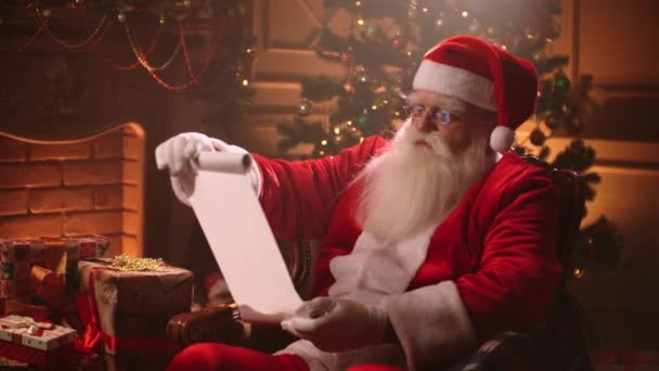 In een magische sfeer leest de Kerstman een papieren rol met een lijst van kinderen voor geschenken. — Stockvideo