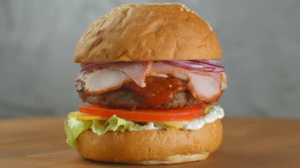 Un hamburger sur une planche, les frites sont éparpillées autour. Gros plan de délicieux hamburger frais fait maison avec laitue, fromage, oignon et tomate sur une planche de bois rustique sur un fond sombre . — Video