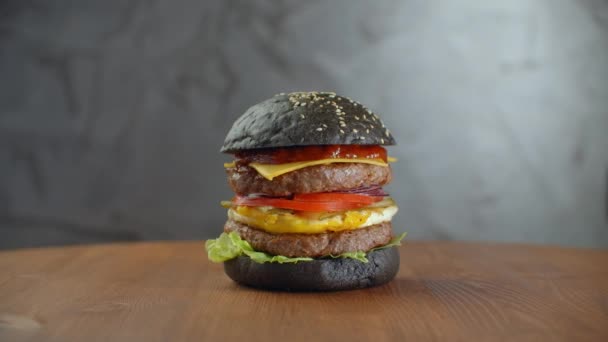 Black burger. A burger with a black roll slices of juicy marble beef, fused cheese, fresh salad and sauce of a barbecue — 图库视频影像