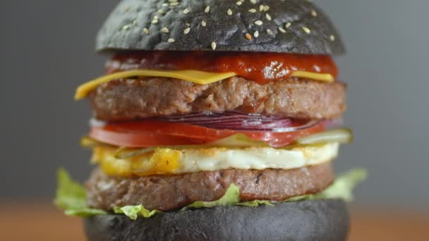 Hambúrguer preto. Um hambúrguer com fatias de rolo preto de carne de mármore suculenta, queijo fundido, salada fresca e molho de um churrasco — Vídeo de Stock