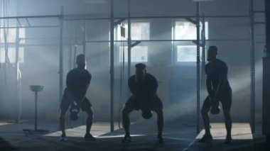 Üç erkek sporcu ağır çekimde kettlebell kaldırarak zorlukların üstesinden geliyorlar. Spor salonunda grup çalışması. Kardiyo eğitimi ve dayanıklılık eğitimi..