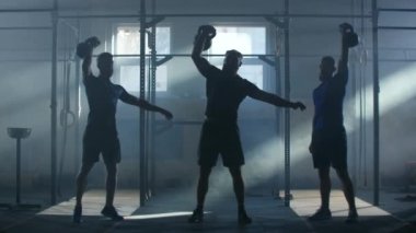 Üç erkek sporcu ağır çekimde kettlebell kaldırarak zorlukların üstesinden geliyorlar. Spor salonunda grup çalışması. Kardiyo eğitimi ve dayanıklılık eğitimi..
