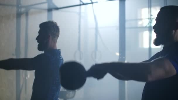 Slow motion: Two man doing exercise with kettlebell. Fitness athletes men training muscular using kettlebell weights doing intense strength exercise friends enjoying weightlifting together in gym. — 비디오