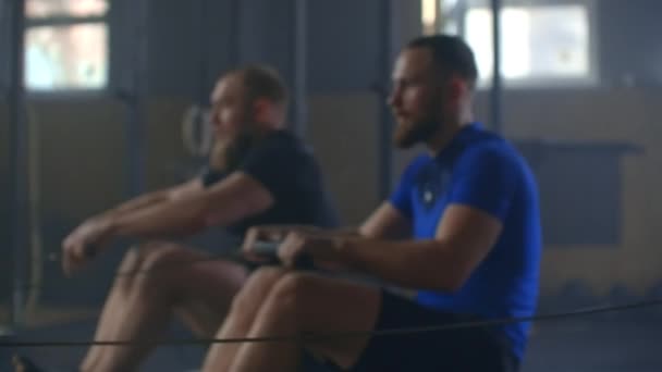Üç güçlü genç adamın kürek çekme makinesi spor salonuyla egzersiz yaparken çekilmesi. Spor salonunda grup erkek atlet eğitimi. Takım çalışması — Stok video