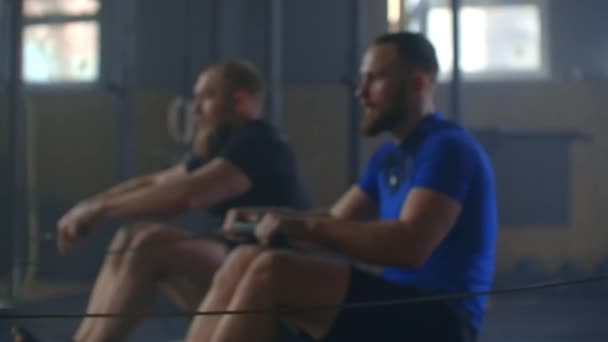 Schuss eines dreiköpfigen jungen Mannes, der mit einem Rudergerät trainiert. Gruppe männlicher Athleten beim Training im Fitnessstudio. Mannschaftstraining — Stockvideo