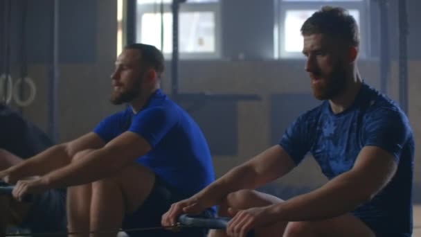 Three men work out together on rowing gym machines slow motion — 비디오