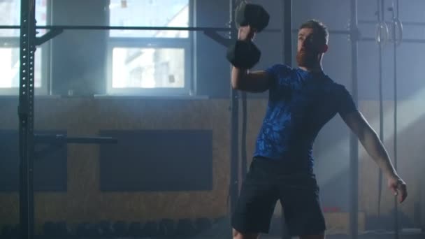 Slow motion: Brutal athlete lifts the Dumbbell above himself, performing a jerk, a spinning push. A man with a beard is engaged in weightlifting on a dark background. — 비디오