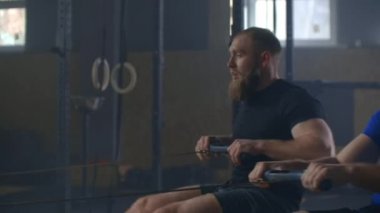 Kürekçiler için ağır çekim takım çalışması. Grup kardiyo eğitimi. Fitness erkek arkadaşları çapraz spor salonunda ergometre makinesinde antrenman yapıyorlar