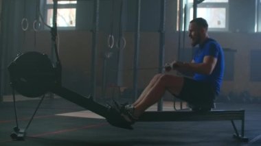Yavaş çekim adamlar spor salonunda egzersiz makineleriyle kürek çekiyorlar ve halat çekiyorlar.
