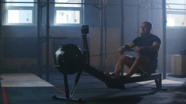 Yavaş çekim adamlar spor salonunda egzersiz makineleriyle kürek çekiyorlar ve halat çekiyorlar.