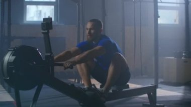 Yavaş çekim adamlar spor salonunda egzersiz makineleriyle kürek çekiyorlar ve halat çekiyorlar.