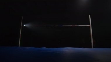 Erkek bir atlet koşuyor ve direğin üzerinden atlıyor. Yüksek atlama yarışmasında yavaş çekim. Profesyonel Olimpiyat sporları