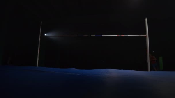 スローモーション:スポットライトの暗い背景に男性選手のハイジャンプ — ストック動画