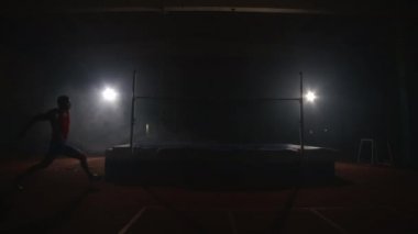 Olimpik sporda bir adam yüksek atlama yapar ve ağır çekimde bir levhayı devirir..