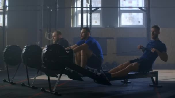 Three men work out together on rowing gym machines slow motion. Team training — 비디오