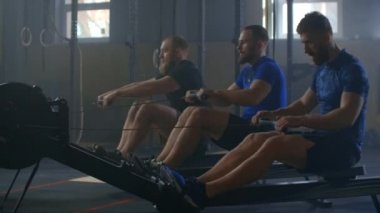 Active and healthy lifestyle, group young athletic happy Caucasian men work out together on rowing gym machines slow motion