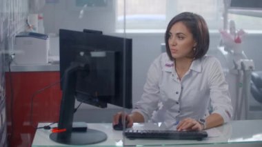 Laboratuvar önlüklü profesyonel kadın doktorun aydınlanmış ofis masasında şeffaf monitörle fütürist bilgisayarda yazı yazması. Ar ögeleri eklemek için uygun video