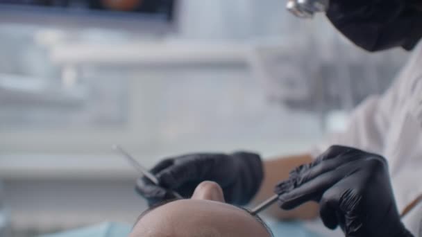 Primo piano di un dentista in binocolo e una maschera che esamina la cavità orale di un paziente sdraiato su una sedia. Il concetto di un sorriso sano — Video Stock