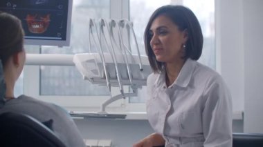 Kadın bir ortodontist dişçi, sandalyesinde oturan bir hastayla MR taramasını tartışıyor.