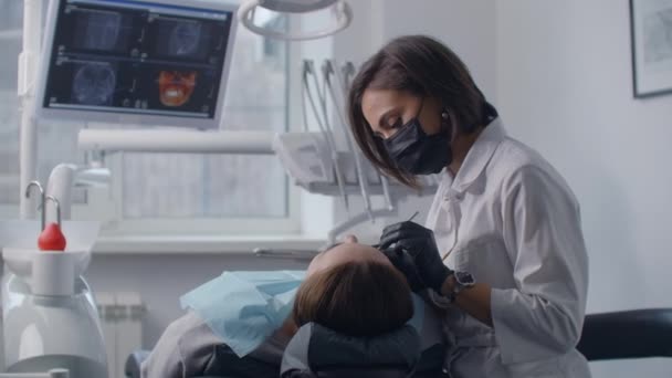 Bir dişçi ekrandaki bir resmin arka planında bir sandalyede yatan bir hastayı tedavi eder. Profesyonel dişçi. — Stok video