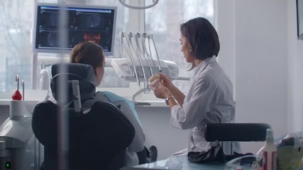 The orthodontist communicates with the patient showing him a cast of teeth and an MRI image — Stock Video