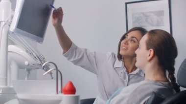 Kadın bir dişçi ekranda MR görüntüsü ve hastaların dişlerinin röntgenini gösteriyor. Tedavi planının tartışılması ve sağlıklı gülümseme.