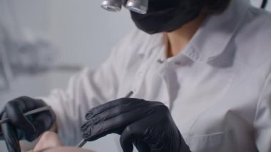 Dürbünlü genç bir dişçi ve beyaz bir ofis bayan bir hastayı muayene ediyor ve tedavi ediyor. Diş tedavisi ve diş tellerinin kurulumu