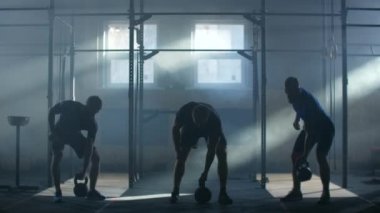Slow motion: Group training Three athletes in an atmospheric fitness room against the background of the rays of sunlight lift up kettlebell