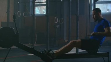 Slow motion: one man in an atmospheric fitness room in the sunlight in a rowing machine. Rower trains