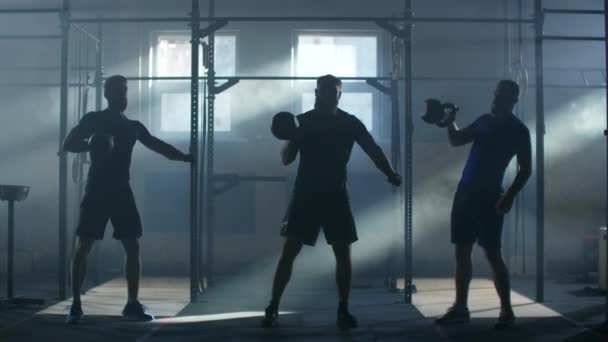 Ralenti : Trois athlètes dans une salle de fitness atmosphérique sur fond de haltères ensoleillées — Video