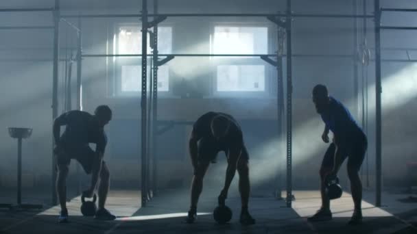 Movimiento lento: Entrenamiento en grupo Tres atletas en una sala de fitness atmosférica contra el fondo de los rayos de luz solar levantan pesas — Vídeo de stock