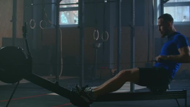 Slow motion: one man in an atmospheric fitness room in the sunlight in a rowing machine. Rower trains — Stok video