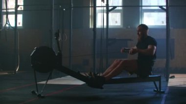 Slow motion: one man in an atmospheric fitness room in the sunlight in a rowing machine. Rower trains, cardio athlete training