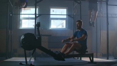 Yavaş çekimde çapraz eğitim, fitness odasında üç adam, arka planda iki adam, bir tanesi kürek makinesi kullanıyor..