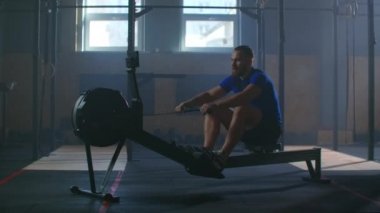 Slow motion: one man in an atmospheric fitness room in the sun in a rowing machine