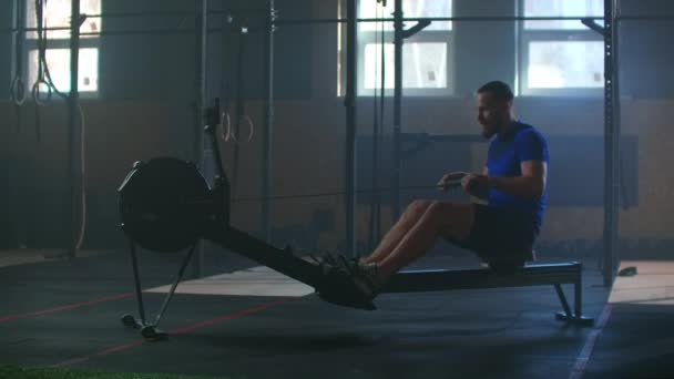 Movimento lento: um homem em uma sala de fitness atmosférica à luz do sol em uma máquina de remo. Trens de remadores, treinamento de cardio atleta — Vídeo de Stock