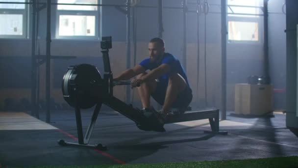 Movimento lento: Trens de remador, treinamento de cardio atleta. Um homem em uma sala de fitness atmosférica à luz do sol em uma máquina de remo . — Vídeo de Stock