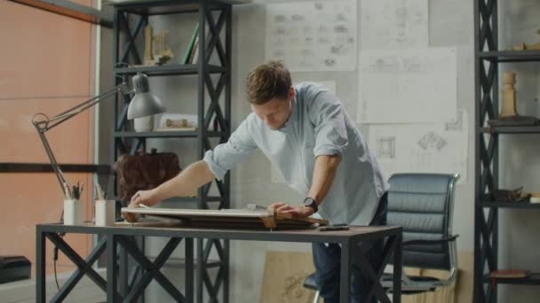 Ingeniero trabaja en una oficina luminosa con una gran ventana, se concentra y dibuja planos. Lugar de trabajo de un arquitecto o diseñador: estilo loft, interior minimalista, dibujos . — Vídeos de Stock