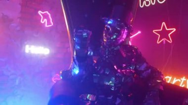 Çelik metalden bir takım elbiseli ve şapkalı bir adam sandalyeye oturur ve kafasını neon ışıkta müzik eşliğinde sallar. Kollarını açar ve dans eder.