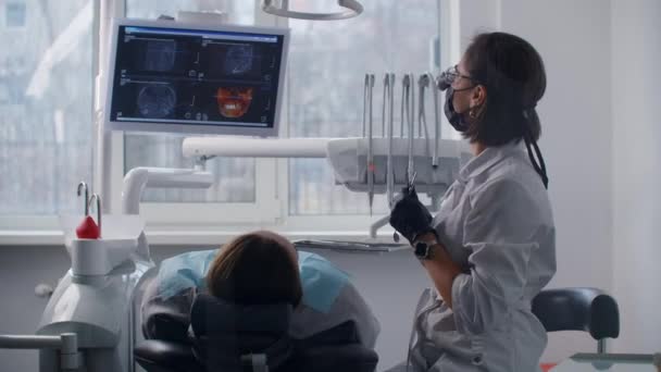 Μια γυναίκα οδοντίατρος ανάβει τη λάμπα και αρχίζει να δουλεύει με τον ασθενή. Σύγχρονη οδοντιατρική κλινική — Αρχείο Βίντεο