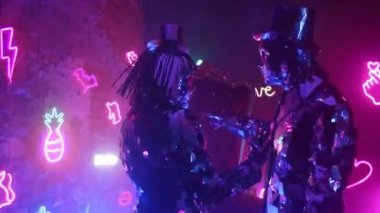 Parlak kostümlü iki robot dansçı birbirlerine yaklaşan neon bir duvara karşı dans ediyorlar.