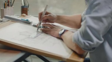 Mühendis büyük bir penceresi olan parlak bir ofiste çalışıyor, konsantre oluyor ve planlar çiziyor. Bir mimarın veya tasarımcının çalışma yeri: tavan arası tarzı, minimalist iç mekan, çizimler.