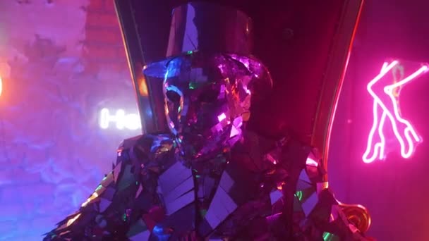 A man in a steel silver metal suit sits in a chair and shakes his head to music in the neon light — Stock Video