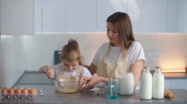 Anne ve kızı kevaşenin içine un ekiyorlar. Anne kızına hamur yoğurmayı öğretiyor. Genç anne asistanı. Ekmek ve turta üretimi için aile işi, aile pastanesi..