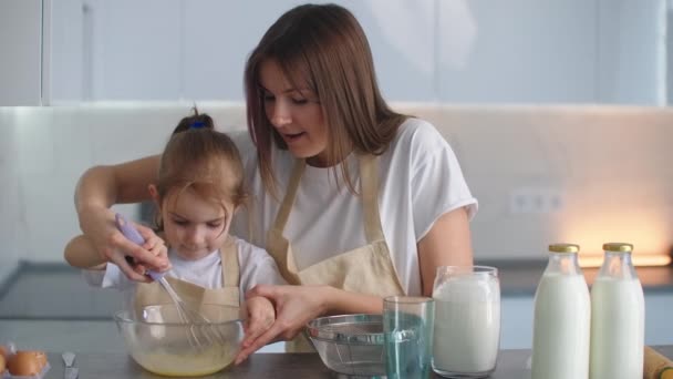 Mama pomaga córce nauczyć się gotować. Razem w fartuchach w kuchni, bić i ugniatać ciasto na przyszłe ciasto i aladiy. Wspólna kuchnia domowa. — Wideo stockowe