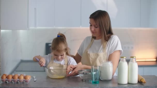 Pembantu ibu kecil. Gadis kecil akan mengalahkan adonan untuk pancake. Ibu mengajarkan anak perempuan untuk memasak . — Stok Video