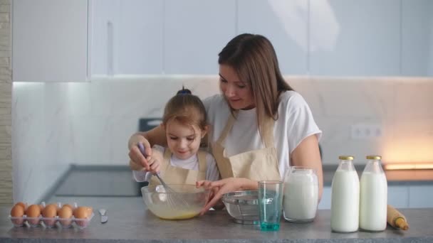 En leende mor hjälper sin dotter lära sig att göra en paj. Lär en liten flicka hemhjälp. — Stockvideo