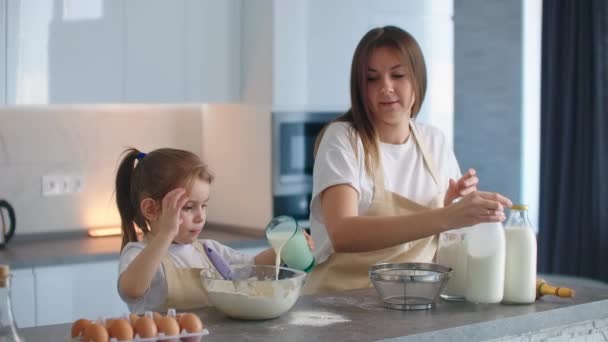 Kız ve anne birlikte yemek pişiriyor. Kadın, yoğurmak için hamura süt döken ellerdir. Annesi küçük bir kızın pasta pişirmeyi öğrendiği bir asistan. Okul öncesi yaşı. — Stok video