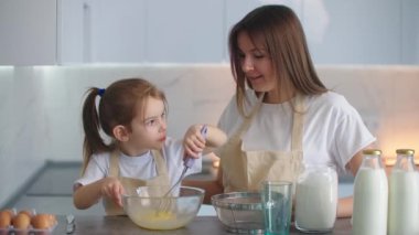 Anne kızına turta yapmak için çırpıcıyla hamur kırbaçlamayı öğretiyor. Sevgili anne ve kızı birlikte turta pişiriyorlar..