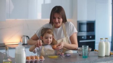 Kadın ve kız mutfakta yumurta çırpıyor. Kız ve anne birlikte yemek pişiriyorlar.